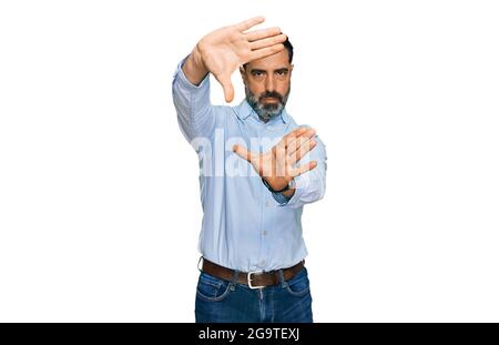 Middle aged man with beard wearing business shirt doing frame using hands palms and fingers, camera perspective Stock Photo