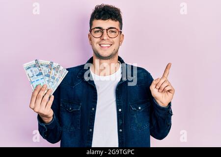 Young hispanic man holding peruvian sol banknotes smiling happy pointing with hand and finger to the side Stock Photo