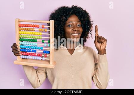 Young african american woman holding traditional abacus smiling with an idea or question pointing finger with happy face, number one Stock Photo
