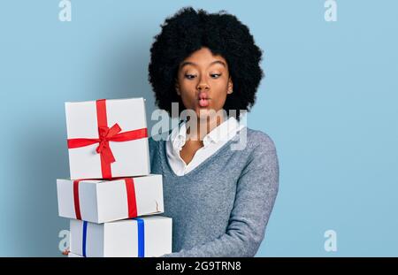 Young african american woman holding gifts making fish face with mouth and squinting eyes, crazy and comical. Stock Photo