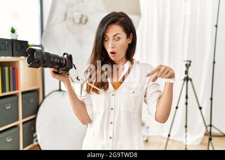 Beautiful caucasian woman working as photographer at photography studio pointing down with fingers showing advertisement, surprised face and open mout Stock Photo