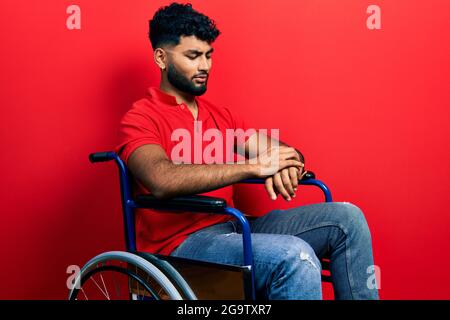 Arab man with beard sitting on wheelchair checking the time on wrist watch, relaxed and confident Stock Photo