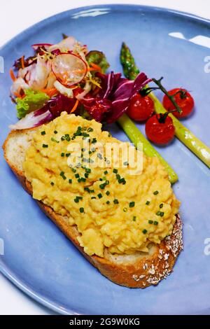 Scrambled eggs on toasted bread with asparagus, tomato and mixed lettuce, summer breakfast Stock Photo