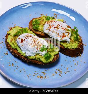 smashed avocado on whole grain toast bread with poached organic eggs on a serving plate Stock Photo