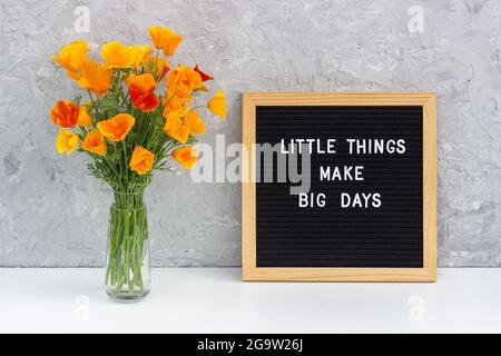 Little things make big days. Motivational quote on letter board and bouquet orange flowers on white table against grey stone wall. Concept inspiration Stock Photo