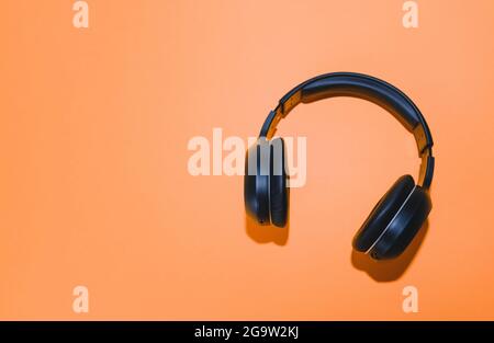 Black wireless headphones isolated on an orange background.  Stock Photo