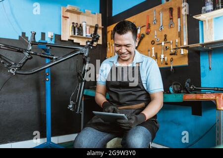a bicycle mechanic sits using a digital tablet to browse Stock Photo