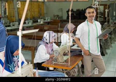 Asian man with measuring tape worn around his neck holding a tablet pc standing Stock Photo