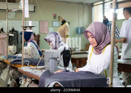 Tailor woman in hijab with a measuring tape worn around her neck using sewing machine at working Stock Photo