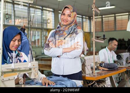 owner in a headscarf smiling with crossed hands stands to the side a tailor Stock Photo