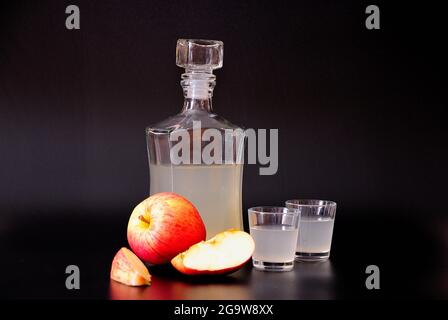 Natural calvados in two ryukas and a glass decanter, ripe cut red apples next to it on a black background. Close-up. Stock Photo