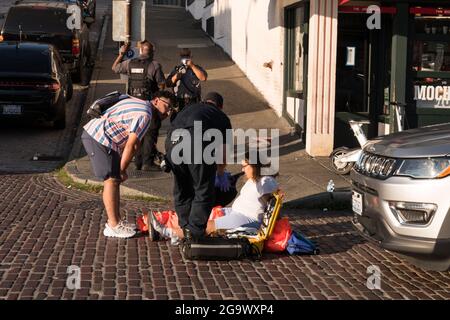 Seattle, USA. 27th Jul, 2021: An injured e-bike bike-share rider at pike place market after a collision with a vehicle late in the day. The new bike share and scooters are not supposed to be ridden on sidewalks, but companies are also not required to provide helmets for riders to comply with local city helmet laws. This puts riders in a tough spot to either ride on sidewalks endangering pedestrians or ride in traffic with vehicles endangering themselves and therefore breaking the helmet laws. Credit: James Anderson/Alamy Live News Stock Photo