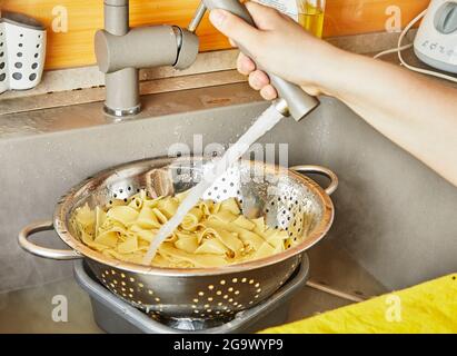 Teenager rinses pasta under running water for spaghetti bolognese according to recipe from the Internet Stock Photo