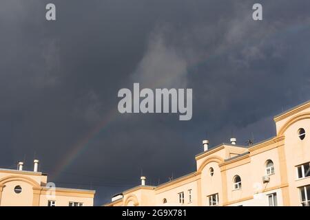 A rainbow over the house against the background of dark storm clouds. The concept of a storm, worsening weather, heavy rain and inclement weather. Sum Stock Photo