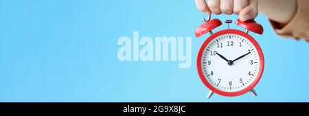 Woman holding red alarm clock in her hand on blue background closeup Stock Photo