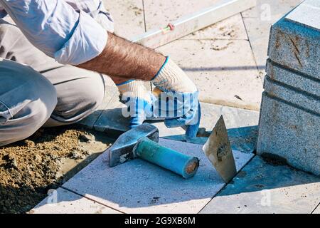 Hands of a Turkish pavement construction worker installing tiles with a trowel and a hammer. Stock Photo