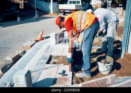 Pavement construction workers installing tiles to build a sidewalk. Stock Photo