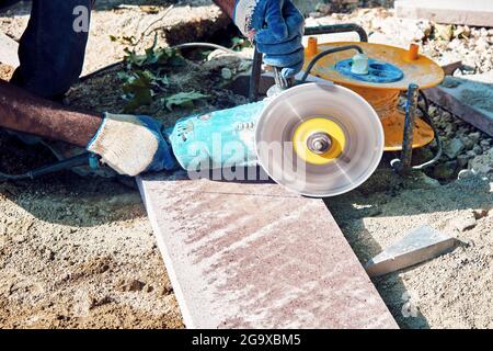 Hands of a pavement construction worker using an angle grinder for cutting the tiles. Stock Photo
