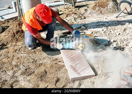 Pavement construction worker using an angle grinder for cutting the tiles. Stock Photo