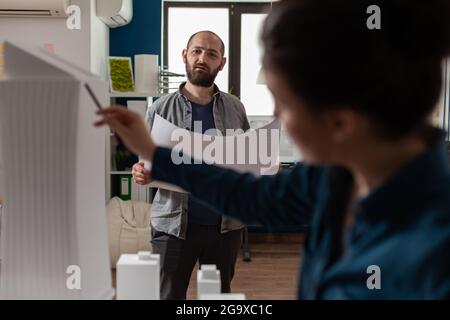 Architecture workers checking blueprints with maquette building model design plan. Caucasian workmates pointing at construction project layout for urban development business Stock Photo