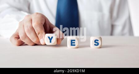 Businessman placing the wooden cubes with the word yes. Stock Photo