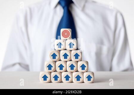 Tiered wooden cubes with arrow icons pointing towards a target. Goal achievement Stock Photo