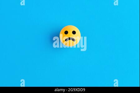 Sad face emoticon or icon on a ball on blue background. Negative feedback concept. Stock Photo