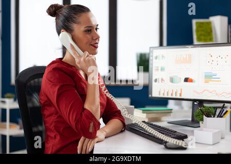 Businesswoman sitting at desk in corporate office discussing with client about important project, during phone conversation. Busy entrepreneur worker discusing contract details. Stock Photo