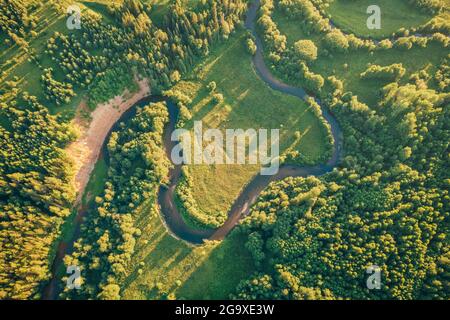 Small narrow winding river, green fields and forest aerial view. Green beautiful rural drone landscape in sunset light. Nature, sustainable and ecology concept. Top down view. Beautiful nature texture Stock Photo