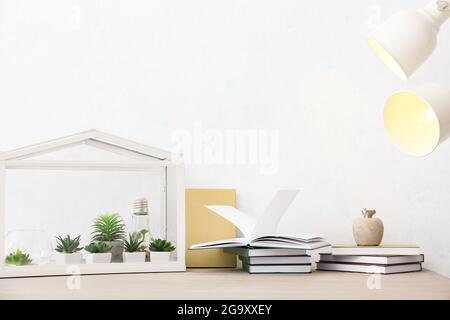 Books and florarium on table near light wall Stock Photo