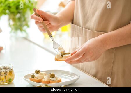 Woman making sandwiches with tasty feta cheese, oil and olives on light table in kitchen, closeup Stock Photo