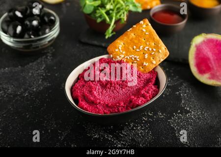 Bowl with tasty beet hummus and cracker on dark background Stock Photo