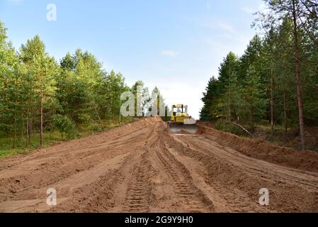 Dozer during clearing forest for construction new road . Yellow Bulldozer at forestry work Earth-moving equipment at road work, land clearing, grading Stock Photo