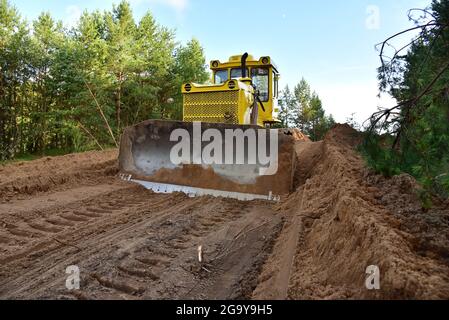 Dozer during clearing forest for construction new road . Yellow Bulldozer at forestry work Earth-moving equipment at road work, land clearing, grading Stock Photo