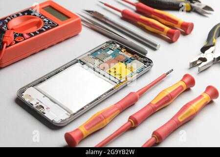 Disassembled mobile phone with technician tools on grey background Stock Photo