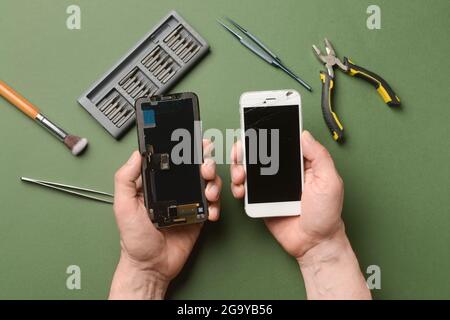 Male technician with disassembled mobile phone and technician tools on color background Stock Photo