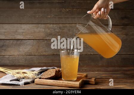 Woman pouring fresh kvass in glass on wooden background Stock Photo