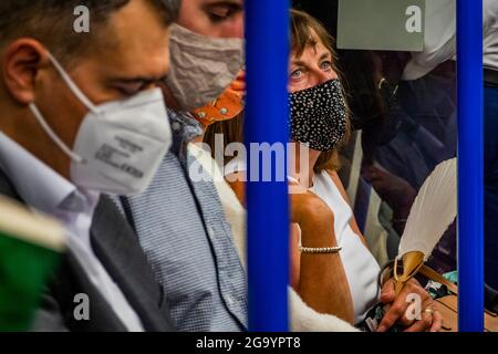 London, UK. 27th July, 2021. A woman brings a fan - Mask confusion continues on the underground after the latest easing, particularly given the increased temperature. The tube is busier and masks are still obligatory but increasing numbers are ignoring the instruction. Credit: Guy Bell/Alamy Live News Stock Photo
