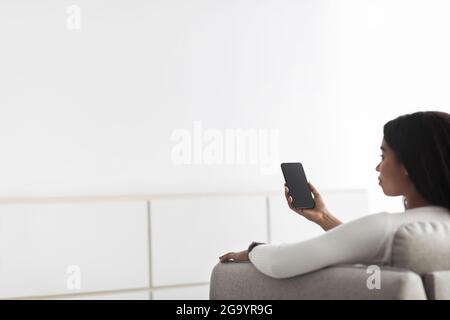 Concept of smart home and mobile application for managing smart devices at home. Black woman controlling home heating Stock Photo