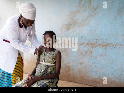 In this image, a black pediatrician with a doctor's suit is placing a stethoscope on the chest of a smiling little girl with typical African braids du Stock Photo