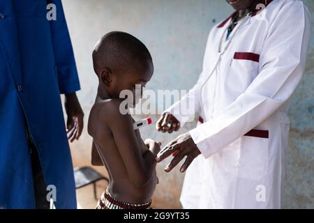 In this image, two medical professionals are checking out the health status of a very skinny black boy undergoing a pre-school examination, among whic Stock Photo