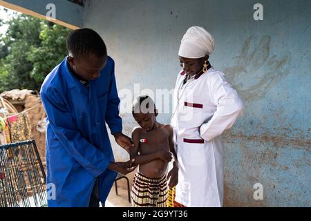 In this image, a young black medical assistenst is taking the temperature of a small toddler during a home visit, under the close supervision of a fem Stock Photo