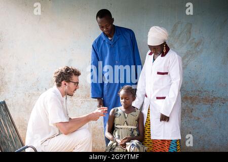 In this image a sitting young caucasian volunteer doctor is explaining a suspicious little African girl how the instrument is working he is going to u Stock Photo