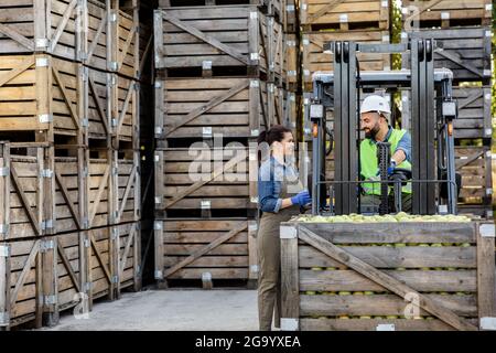 Manager and driver work in warehouse with many wooden boxes, load boxes of fruit for storage Stock Photo