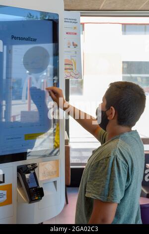 Mallorca, Spain, 07-27-2021: Close-up portrait of a young man doing and ordering in Macdonalds restaurant, using the tounh display panel, Stock Photo