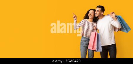 Great Offer. Excited young arab spouses with bright shopping bags pointing aside Stock Photo