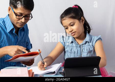 An Indian girl student studying with tablet besides her father, teacher: private teacher concept Stock Photo