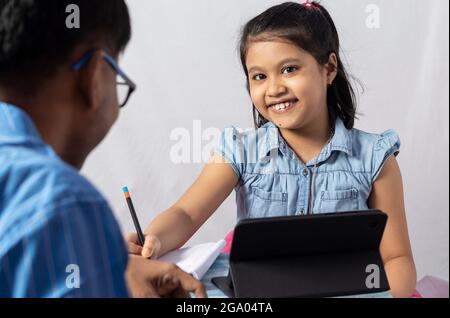 An Indian girl student studying and having fun with tablet in front of her father, teacher: private teacher concept Stock Photo