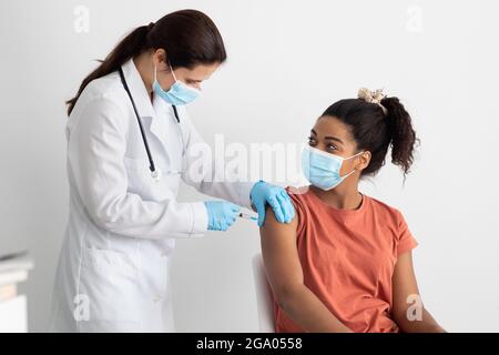 Nurse in white workwear making vaccination for black lady Stock Photo
