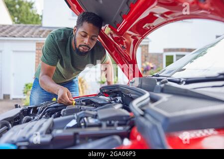 Man Working Under Hood Checking Car Engine Oil Level On Dipstick Stock Photo